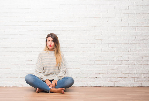 Młoda kobieta dorosłych, siedząc na podłodze biały cegła mur w domu sceptykiem i rozstrój nerwowy, zmarszczenie brwi z powodu problemu. Negatywne osoba. - Zdjęcie, obraz