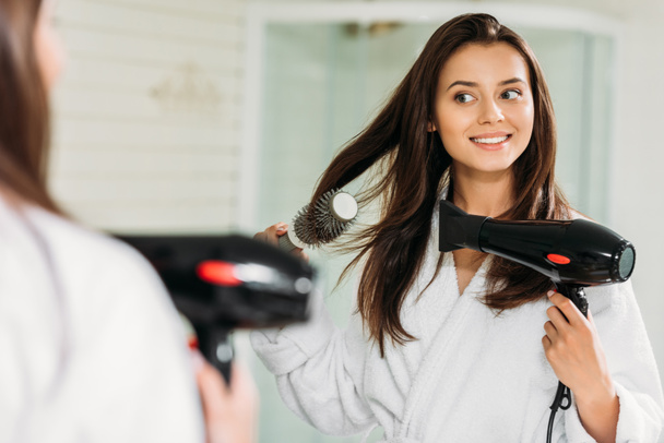 happy young woman drying hair at mirror in bathroom  - Foto, Bild