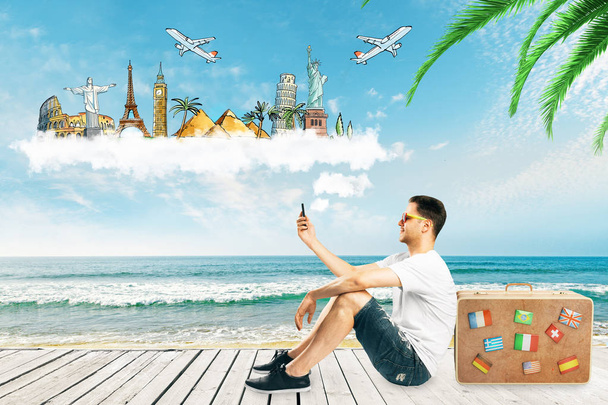 Alkalmi fiatal európai ember smartphone, poggyász és utazási vázlat a kék ég háttér. Utazás és a tengerparti koncepció  - Fotó, kép