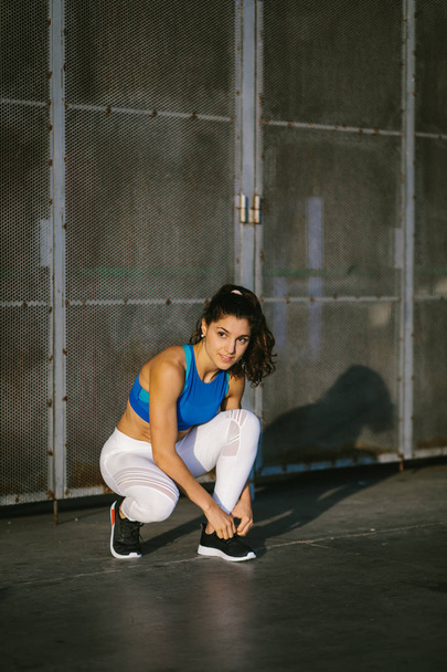 Young sporty female athlete lacing footwear and getting ready for urban running and fitness workout. Motivated woman training outside. - 写真・画像