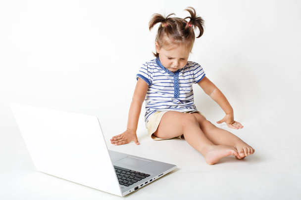 Childhood in digital age. Attractive little kid sneezes and has eyes shut, looks down, sits near portable laptop computer, isolated over white background. Children and modern technologies concept - Foto, Imagen