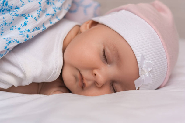 Close up portrait of adorable lovely baby sleeps calmly in bed, covered with warm blanket, has pleasant healthy sweet dream, cared by affectionate parents. Infant care and childhood concept. - Zdjęcie, obraz