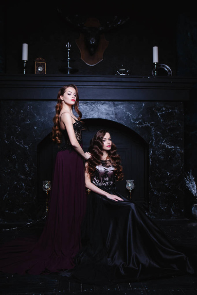 Twins young women in evening dresses, fashion beauty portrait in dark interior - Photo, image
