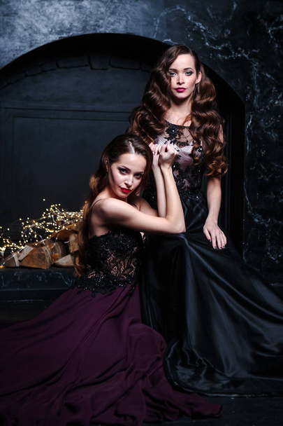 Twins young women in evening dresses, fashion beauty portrait in dark interior - Zdjęcie, obraz