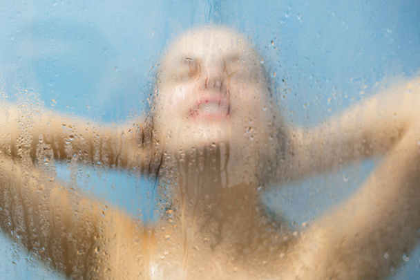 Naked woman stands in douche, takes shower under hot water, feels relaxed, has clean body. Water drops on background. Body and skin hygiene. Woman takes bath in bathroom. Relaxation concept. - Photo, image