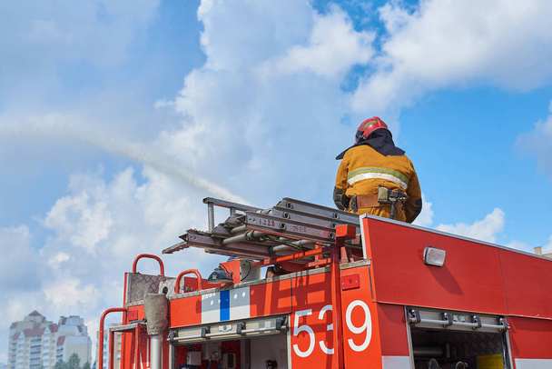 Pompier sur le toit d'un camion de pompiers arrosant à partir d'un tuyau d'incendie
 - Photo, image
