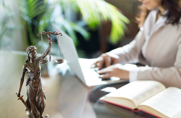 Escritório de advogados. Estátua da Justiça com escalas e advogado trabalhando em um laptop. Direito jurídico, aconselhamento e conceito de justiça
 - Foto, Imagem
