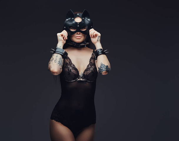 Seductora sensual amante chica con lencería negra en accesorios BDSM y máscara de cuero para gatos posando sobre un fondo oscuro. Aislado sobre un fondo oscuro
.    - Foto, imagen