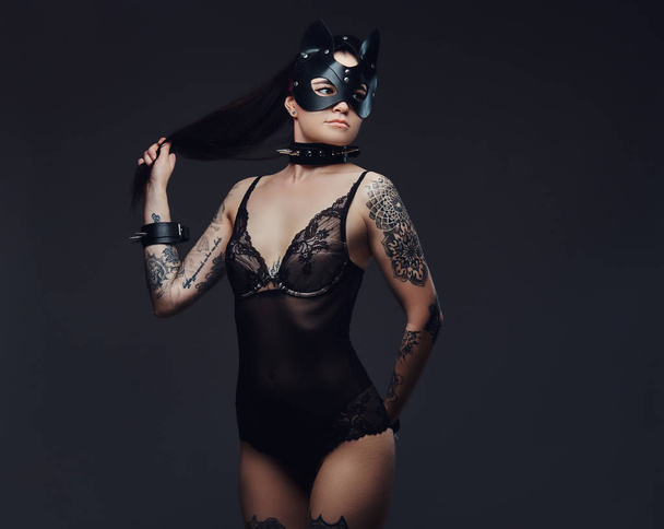 Σέξι γυναίκα που φοράει μαύρα εσώρουχα σε Bdsm γάτα δερμάτινη μάσκα και αξεσουάρ θέτοντας σε σκούρο φόντο.  - Φωτογραφία, εικόνα