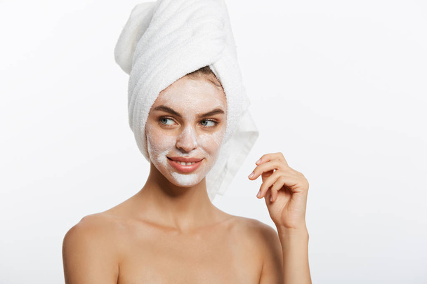 若い女性が彼女の顔に保湿クリームを適用します。白いバスローブとタオルの白い背景の上の女性の写真。肌ケアのコンセプト - 写真・画像