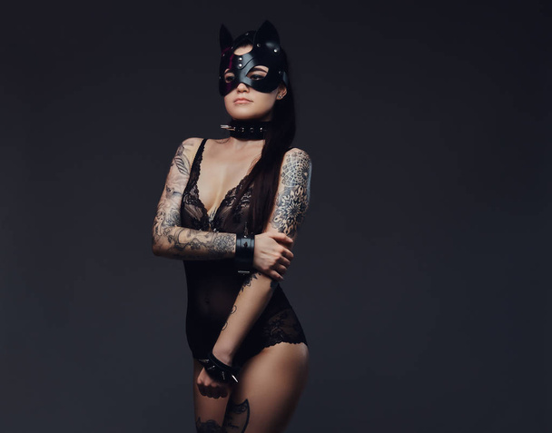 schöne brünette Frau trägt sexy schwarze Dessous in bdsm Katzenledermaske und Accessoires posiert auf einem dunklen Hintergrund.  - Foto, Bild