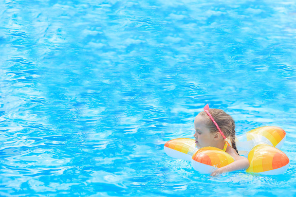 Happy little girl playing with colorful inflatable ring in outdoor swimming pool on hot summer day. Kids learn to swim. Child water toys. Children play in tropical resort. Family beach vacation. - Photo, Image