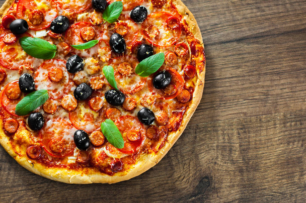 Pizza z serem Mozzarella, salami, papryka, pepperoni, pomidory, oliwki, przyprawy i świeżą bazylią. Włoskiej pizzy na podłoże drewniane. z miejsca kopii. Widok z góry - Zdjęcie, obraz