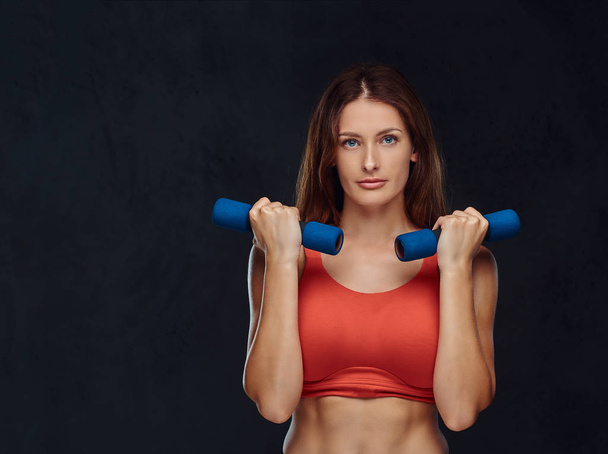 Mujer fitness vestida con sujetador deportivo haciendo ejercicio con pesas. Aislado sobre un fondo de textura oscura
. - Foto, imagen