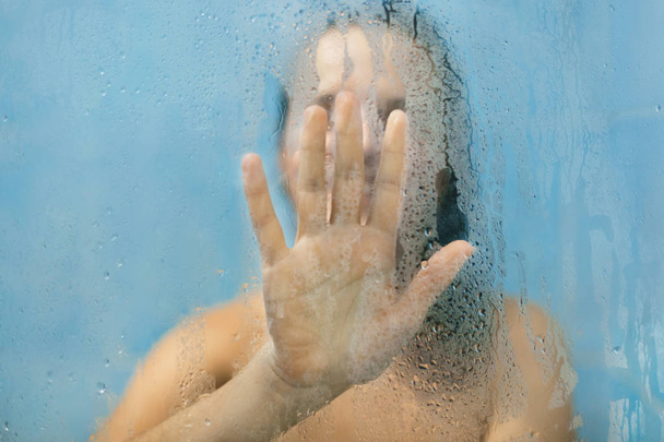 Female`s palm on blurred sweat glass of shower cabine door. Unrecognizable woman touches glass while takes shower, has naked body, relaxes after hard woking day. Hygienics and cleaning concept - Foto, Imagem