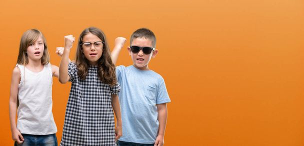 Skupina chlapce a dívky děti oranžové pozadí naštvaný a frustrovaný křičí s hněvem, šílený a křičel zvedl ruku, hněv koncepce - Fotografie, Obrázek
