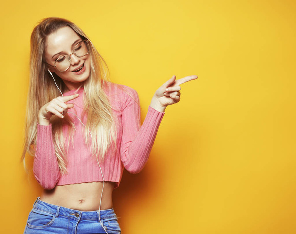 lifestyle and people concept - Portrait of a pretty blond girl pointing finger away over yellow background - Foto, imagen