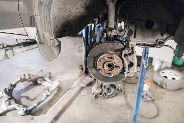 Auto monteur inspecteren auto wiel en reparatie schorsing detail. Opgeheven auto bij de reparatiedienst. vervanging van ferrule en leverage - Foto, afbeelding