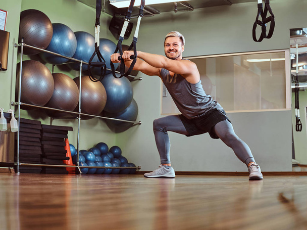 Hombre guapo en ropa deportiva haciendo ejercicio con correas de suspensión en el gimnasio
. - Foto, imagen