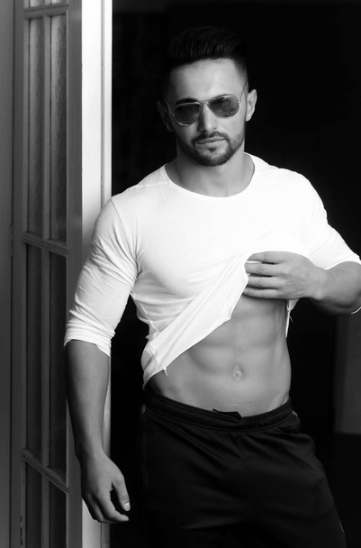 macho man in sunglasses and sportswear showing muscular belly - Foto, afbeelding