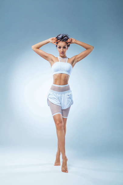 Attractive excited fitness girl dancer in sportwear dance isolated over blue background. Fashion and livestyle concept. - 写真・画像
