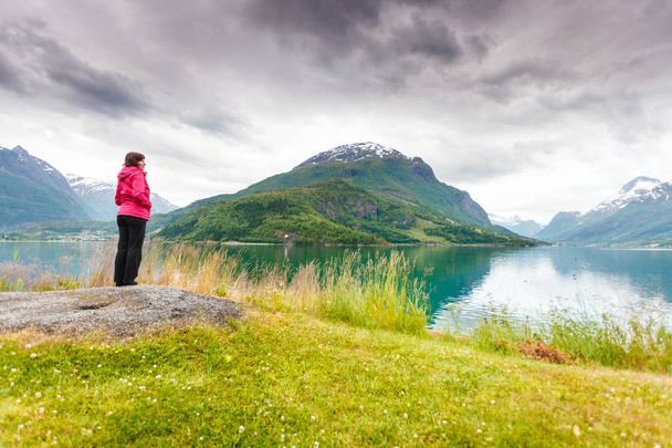 Travel concept. Mature tourist woman on sea shore looking at fjords beautiful landscape, in Olden village, Sogn og Fjordane county Norway. - Zdjęcie, obraz