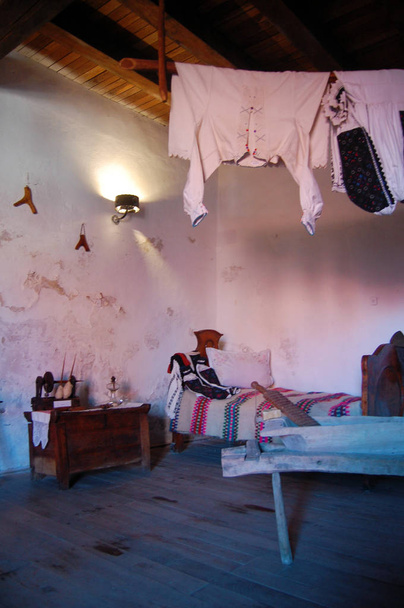 Oud huisje Binnenaanzicht, vintage kleding, bed en huishoudelijke voorwerpen in interieur - Foto, afbeelding