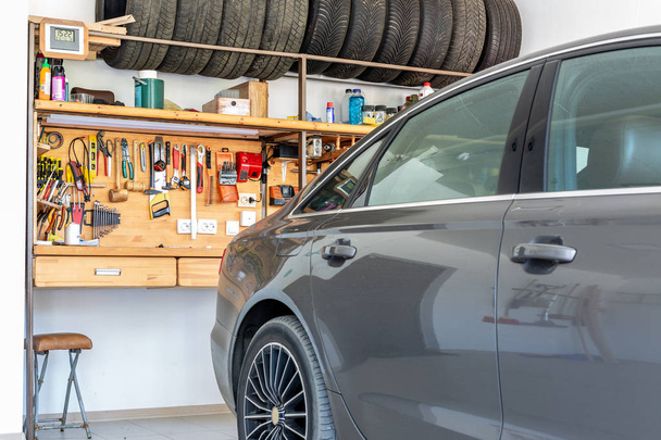 Luxury car parked at large spacious private home garage. Big wooden workbench with lot of tools at background. Spare season wheels storage. DIY, self service and repair - Fotó, kép