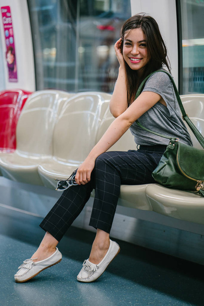 young and pretty Japanese Asian tourist woman sitting on a train in Asia while on vacation. She is cute, attractive and is smiling happily as she relaxes in her seat. - Foto, Bild