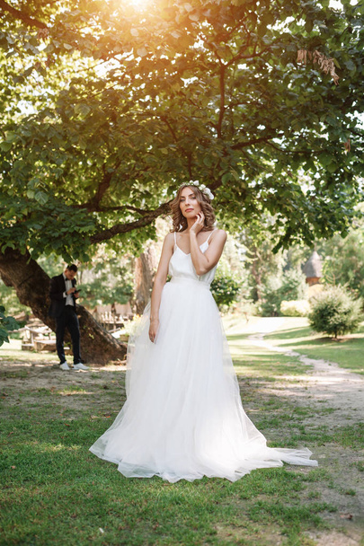 Chica joven con un vestido blanco en el prado. Mujer en un hermoso vestido largo posando en el jardín. Impresionante novia en un vestido de novia
 - Foto, imagen