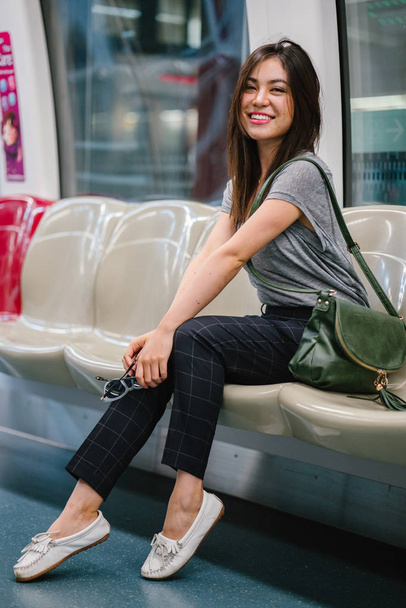 young and pretty Japanese Asian tourist woman sitting on a train in Asia while on vacation. She is cute, attractive and is smiling happily as she relaxes in her seat. - Photo, Image