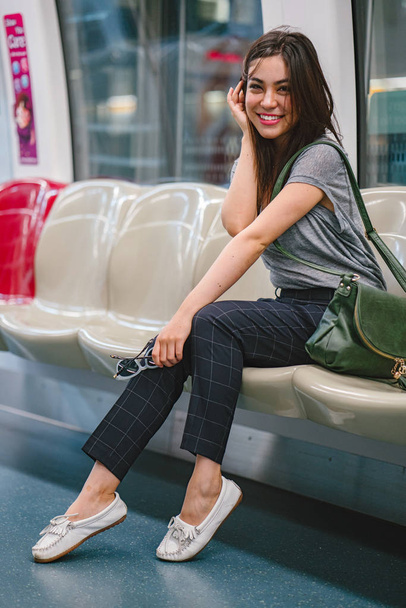 young and pretty Japanese Asian tourist woman sitting on a train in Asia while on vacation. She is cute, attractive and is smiling happily as she relaxes in her seat. - Valokuva, kuva