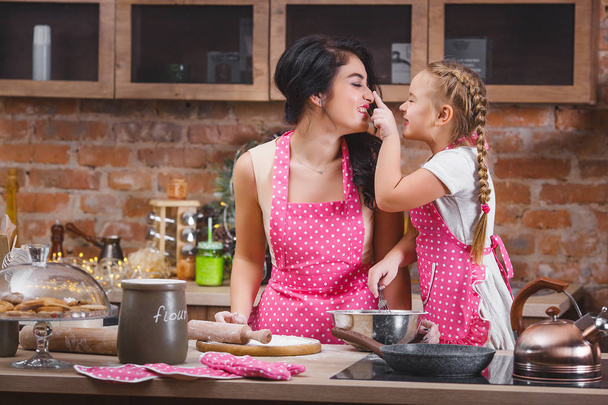 Young beautiful mother and her little daughter cooking together at the kitchen - Photo, Image