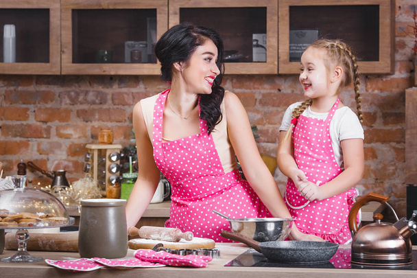 Молодая красивая мать и ее маленькая дочь готовят вместе на кухне
 - Фото, изображение