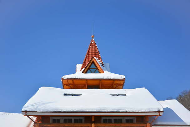 Lunta puutalon katolla. Ullakko ikkuna kolmion muotoinen lumipeitteinen katto taustalla kirkkaan sininen taivas. Aurinkoinen talvipäivä
. - Valokuva, kuva