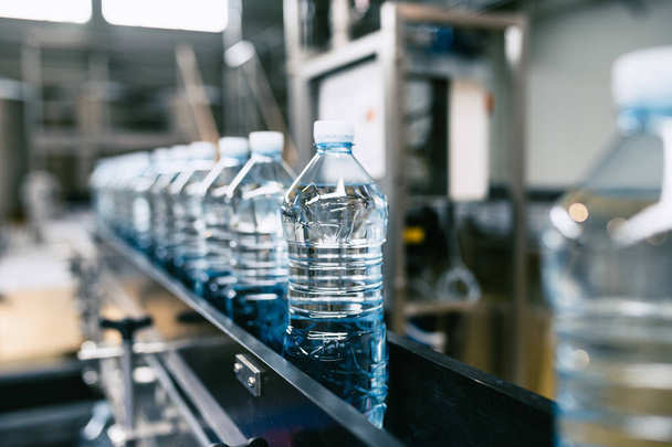 瓶詰め工場-純泉水をブルーボトルに加工および瓶詰めするための水ボトリングライン。選択的焦点.  - 写真・画像