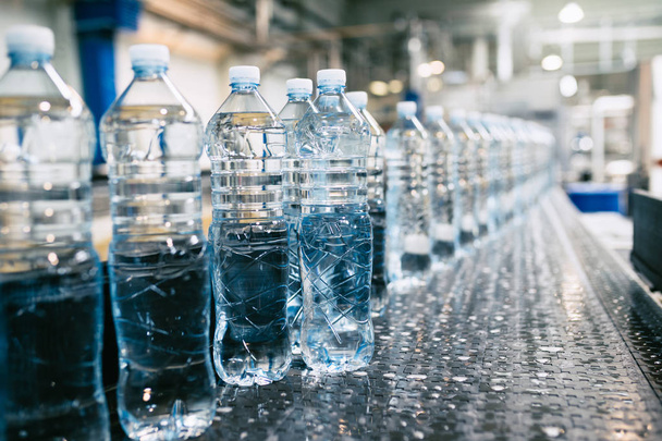 Bottelarij - Waterbottellijn voor het verwerken en bottelen van zuiver bronwater in blauwe flessen. Selectieve focus.  - Foto, afbeelding