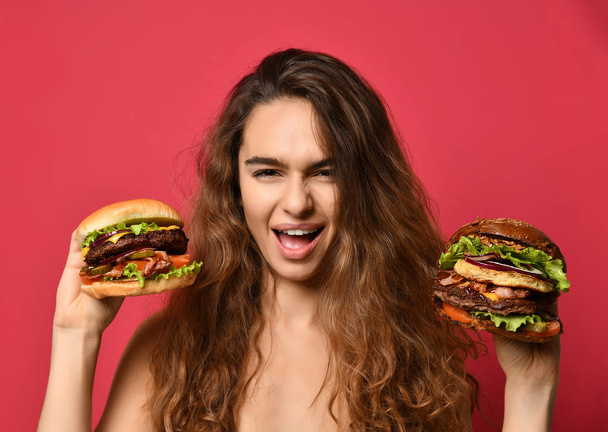 Woman hold two burgers sandwich in hands compare with hungry mouth on pink red background - Valokuva, kuva