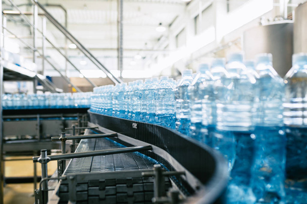 Rozlewnia - linia do butelkowania wody do przetwarzania i butelkowania czystej wody źródlanej w niebieskie butelki. Skupienie selektywne.  - Zdjęcie, obraz