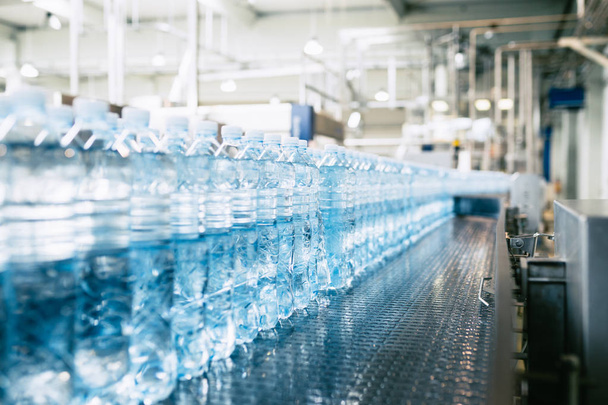 Şişeleme tesisi - Su şişeleme hattı saf kaynak suyunu işlemek ve şişelemek için mavi şişelere. Seçici odak.  - Fotoğraf, Görsel
