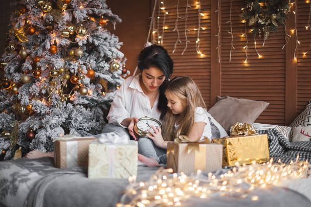 Jonge mooie moeder en haar dochtertje delen Kerst presenteert - Foto, afbeelding