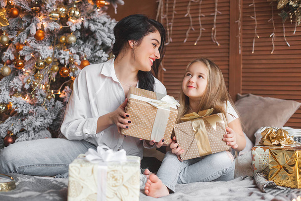 Jovem mãe bonita e sua filhinha compartilhando presentes de Natal
 - Foto, Imagem