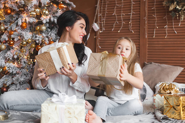 Jovem mãe bonita e sua filhinha compartilhando presentes de Natal
 - Foto, Imagem