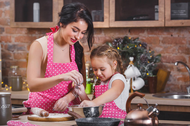 Young beautiful mother and her little daughter cooking together at the kitchen - Photo, Image
