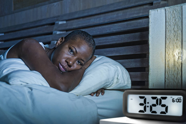 lifestyle portrait of young sad and depressed black afro American woman awake on bed sleepless suffering insomnia sleeping disorder and anxiety problem with alarm clock late night hour - Photo, Image