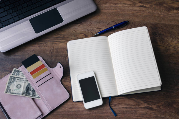 notebook com uma caneta, uma bolsa com dinheiro e cartões de desconto, um laptop e um telefone, em um fundo de madeira
 - Foto, Imagem