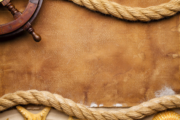 Ship's steering wheel, hawser and seashell on paper and sand background - Photo, image