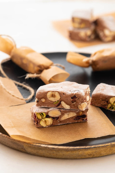 A variety of different nutty nougat in dark chocolate with roasted hazelnuts cut open to show the nougat mix on a wooden board . Copy space. - Foto, immagini