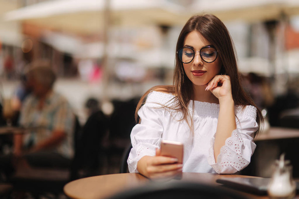 junge fröhliche Frau liest elektronisches Buch auf dem Smartphone, während sie auf ihre Bestellung wartet - Foto, Bild