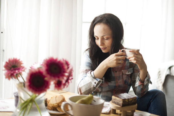 Mujer con una taza de café, un buen día en casa. Desayuno y café perfumado. El interior es acogedor y las flores. Espacio libre para texto
 - Foto, imagen